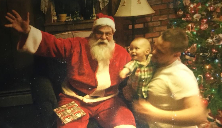A baby reaching up to Santa Claus during a home Christmas visit on the North Shore